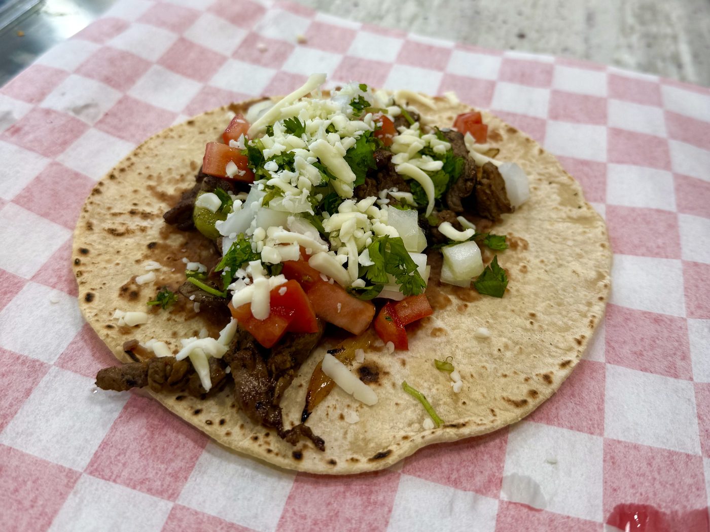 Steak street taco with cilantro, onion, tomato and cheese on a checkered paper liner